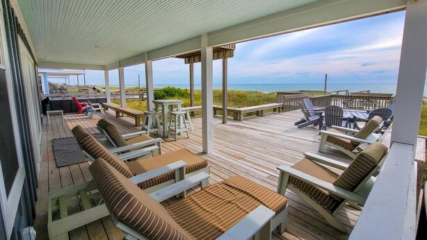 A covered outdoor deck with lounge chairs and tables, overlooking a beach. - Barnacle: Pet-Friendly Ocean Escape (Topsail Beach)