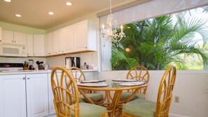 A kitchen with white cabinets, a microwave, and a dining area with wicker chairs and a glass table. - Hale Kamaole 177 Ground floor condo, easy access to best beach on Maui! (Kihei)