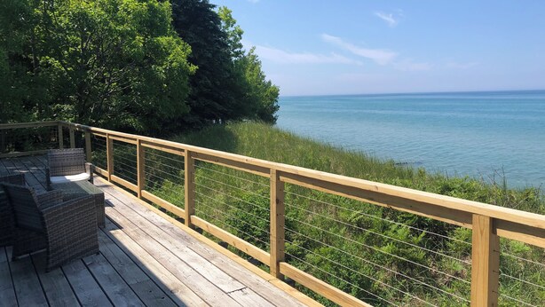 Une terrasse en bois, meublée de meubles en osier, donnant sur une étendue d’eau et entourée de verdure.
