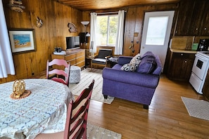 Ein Interieur einer Holzhütte mit Esstisch, Sofa, Fernseher und Küchenzeile.