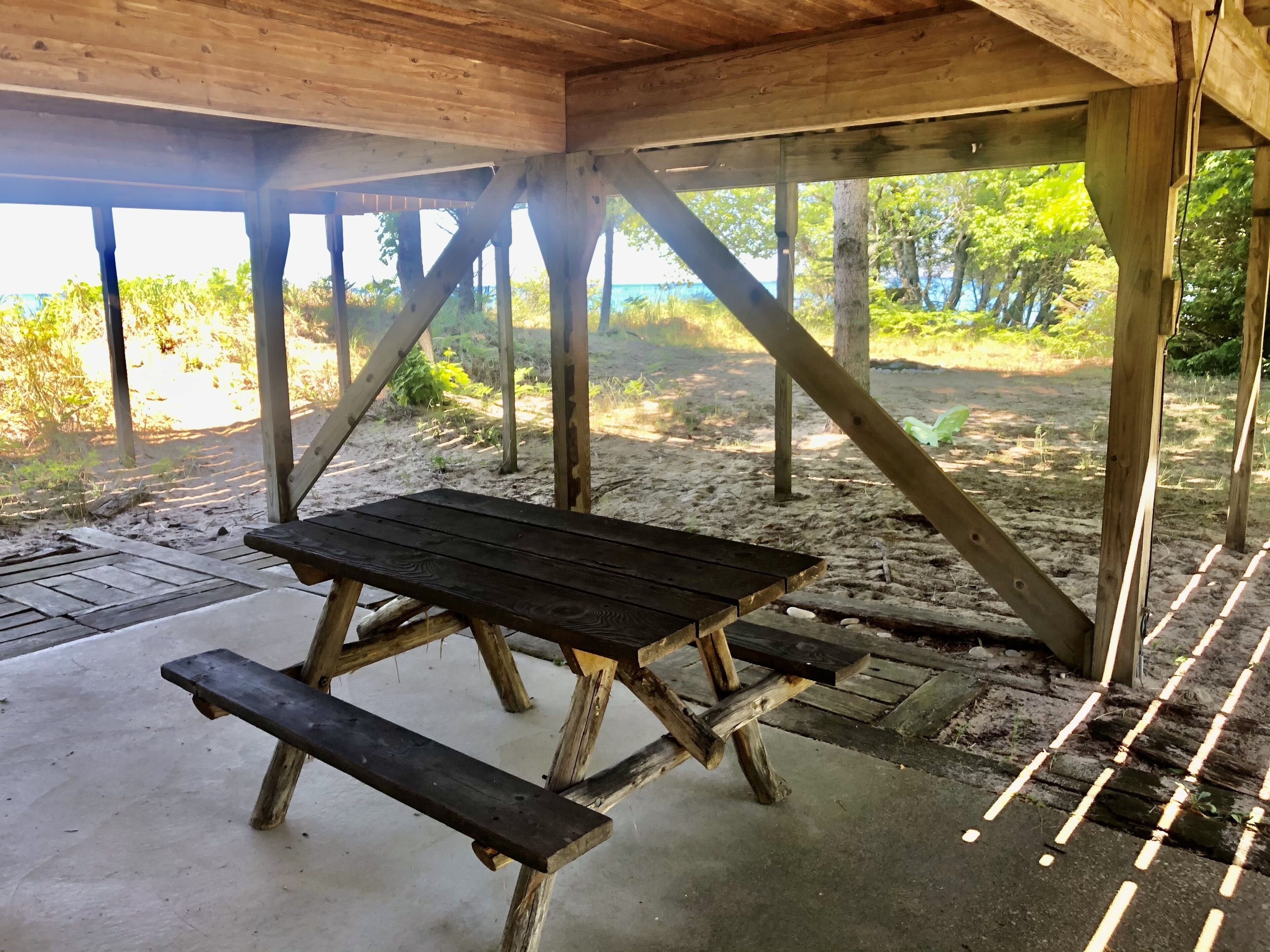 Une table de pique-nique en bois, placée sous un abri, d’où l’on peut admirer la plage et les arbres.