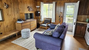 L'intérieur d'un chalet en bois, avec un canapé, une télévision, une lampe et un coin cuisine.