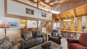 A spacious living area with a high ceiling, wooden beams, a fireplace, and a dining area with a wooden table and chairs.