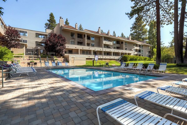 A pool area with lounge chairs and a building with multiple balconies in the background.