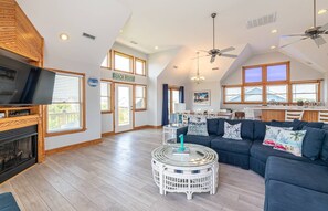 A spacious living room with a large dark blue sofa, a white wicker coffee table, and a flat-screen TV. - On Island Time - KDH MP 7, 275 Yds to Beach, Pool, Hot Tub, Pool Table, Flex Stays (Kill Devil Hills)