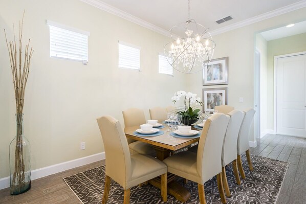 A dining room with a wooden table, beige chairs, a chandelier, and a patterned rug.