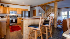 Eine Küche mit Holzausbau, einem Edelstahl-Kühlschrank und einer Mikrowelle. Eine Holztreppe führt zu einer weiteren Ebene.