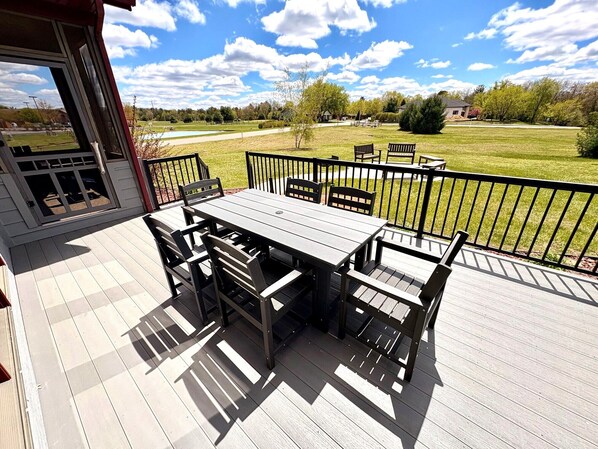 A deck with a table and chairs, a view of a park, and a building in the background.