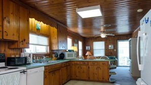 A wooden cabin-style kitchen with a central island, built-in appliances, and a sliding glass door leading to a balcony. - Historic Cottage Across the Street from Beach (Carolina Beach)