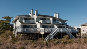 A multi-story beachfront house with a balcony, a staircase leading to the main entrance, and a clear view of the ocean. - 3BR Ocean Front Condo Near Johnnie Mercer’s! (Wrightsville Beach)