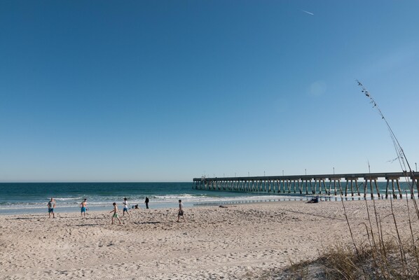 A beach with a pier extending into the water, sandy beach, and people walking.