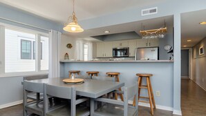 A modern kitchen with a central island, bar stools, and a dining table. - 3BR Ocean Front Condo Near Johnnie Mercer’s! (Wrightsville Beach)