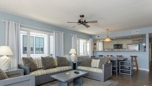 A modern living room with a sofa set, a coffee table, and a dining area with bar stools. - 3BR Ocean Front Condo Near Johnnie Mercer’s! (Wrightsville Beach)