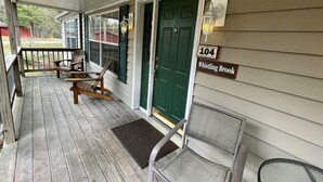 A porch with wooden chairs and a bench, a green door, and a house number sign. - Whistling Brook @ Spring Brook Resort (Wisconsin Dells)