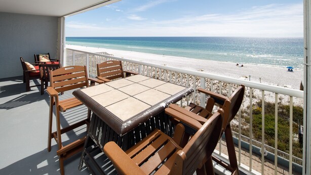 A balcony with a table and chairs overlooking a beach.