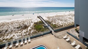 A beach view from a balcony with a pool and sun loungers.