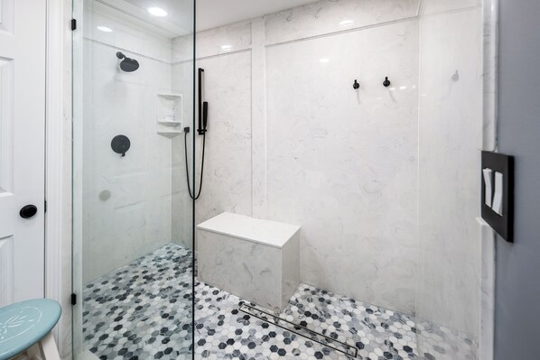 Un baño moderno con ducha de vidrio, lavamanos pedestal blanco y piso de baldosas con diseño geométrico.