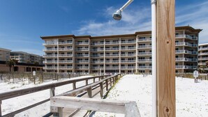 Un muelle de madera que conduce a un hotel frente a la playa con varios balcones y una playa de arena.