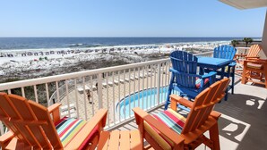 Un balcón con sillas Adirondack anaranjadas, una piscina y vista a la playa.