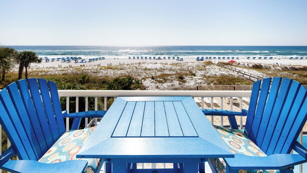 Vista de una playa con una mesa y sillas, una terraza de madera y una playa de arena con sombrillas.