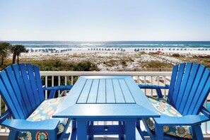 Vista de una playa con una mesa y sillas, una terraza de madera y una playa de arena con sombrillas.
