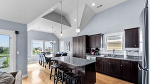 A modern kitchen with dark wood cabinets, a granite countertop, and a large island with bar stools. - Pier Pressure At SandCastle Nags Head Village, Private Pool, On the Golf Course (Nags Head)