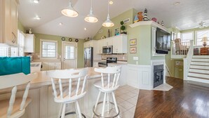 A kitchen with white bar stools, a dining table, a microwave, a refrigerator, and a fireplace. - Mayflower - Corolla, Ocean Sands, 250 Yds to Beach, Lake View, Pool, Hot Tub, Flex Stays (Corolla)
