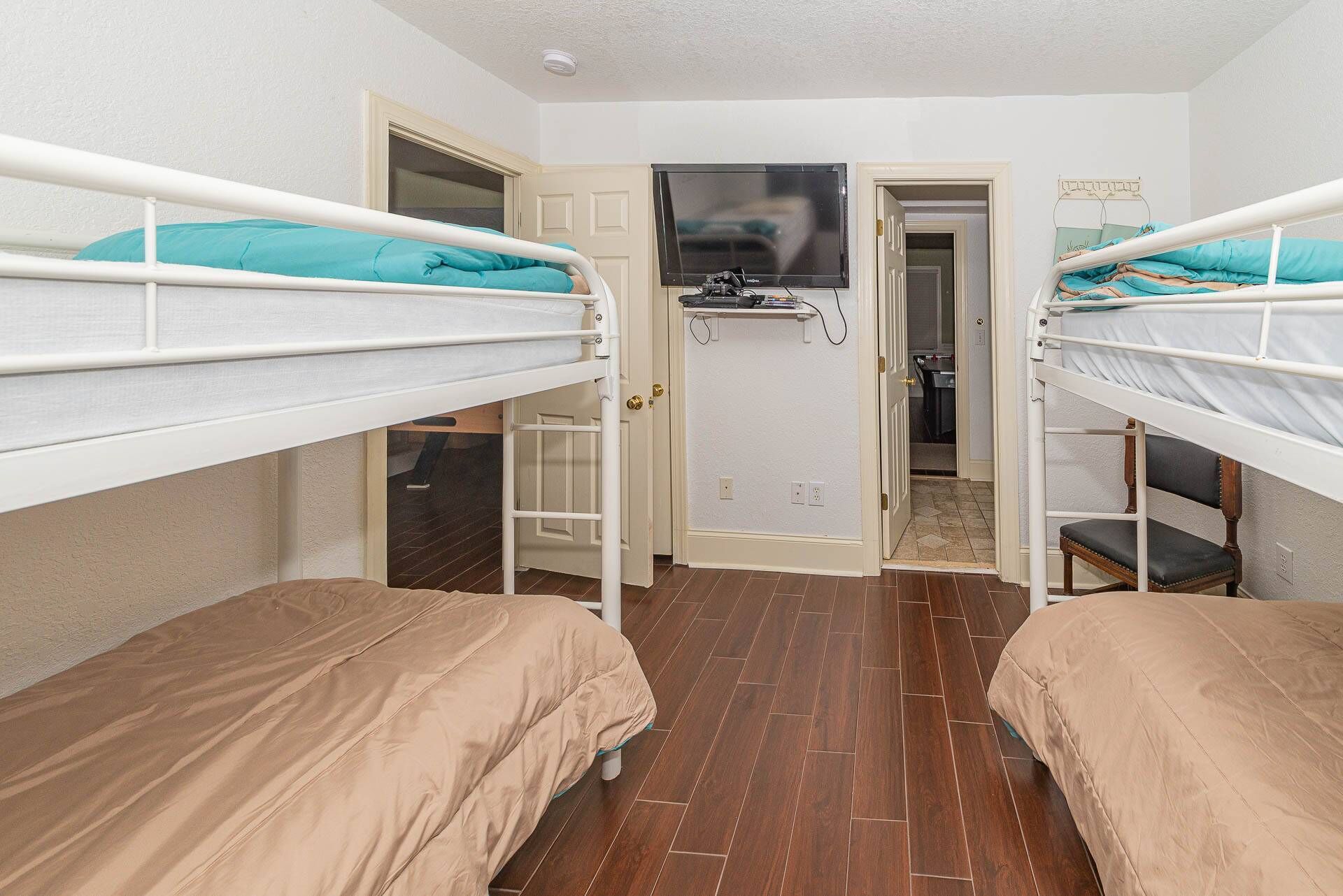 A dormitory room with two bunk beds, a television on a stand, and a door leading to a bathroom.