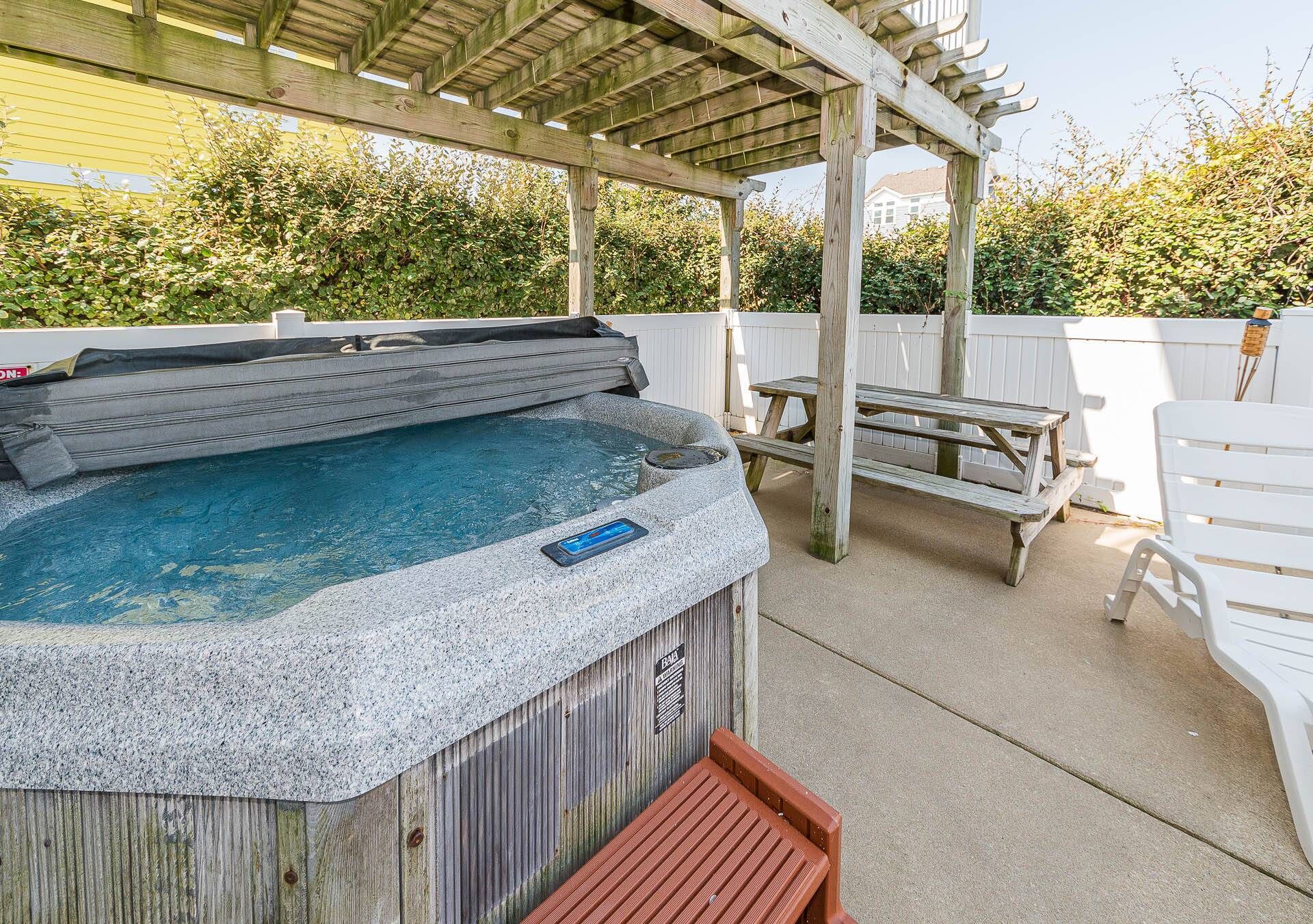 Ein Whirlpool unter einer Holz-Pergola mit einem Picknicktisch und Sitzbänken in der Nähe.