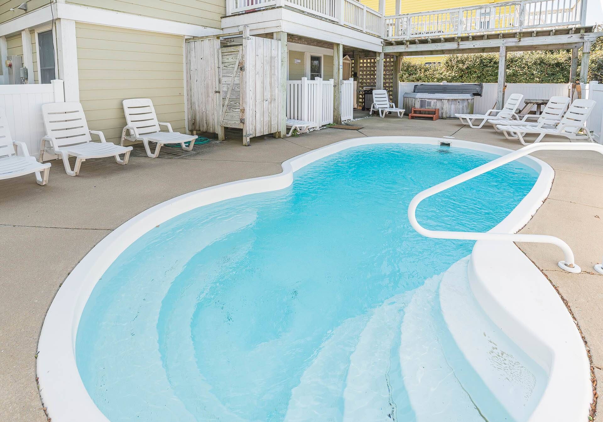 Une piscine entourée de chaises longues blanches et dotée d’un patio couvert.