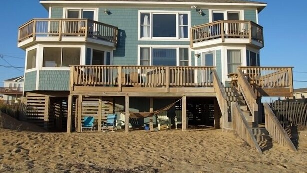 A multi-story beachfront house with a balcony on each floor, wooden railings, and a staircase leading to the upper levels. - KH5203- Oceanfront With Two Masters, Hot Tub, Covered Porch and Dog Friendly! (Kitty Hawk)