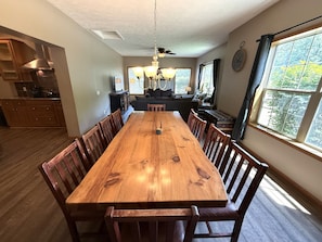 Uma sala de jantar com uma mesa e cadeiras de madeira, uma cozinha com armários e fogão, e uma área de estar com sofá e janela.