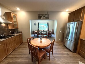 A kitchen with wooden cabinets, a stainless steel refrigerator, a dining table with chairs, and a sign above the table. - Chocolate Moose Lodge @ Spring Brook Resort (Wisconsin Dells)