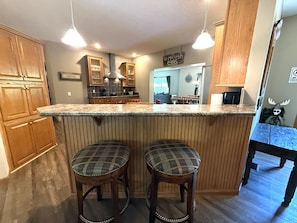 A kitchen with wooden cabinets, a granite countertop, two plaid bar stools, and pendant lighting. - Chocolate Moose Lodge @ Spring Brook Resort (Wisconsin Dells)