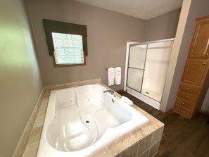 A bathroom with a large bathtub, a shower with a glass door, and wooden cabinets. - Chocolate Moose Lodge @ Spring Brook Resort (Wisconsin Dells)