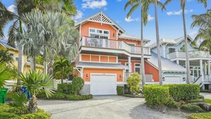 A multi-story house with a white garage, surrounded by palm trees and well-maintained landscaping. - Beautiful Home Two Houses from the Beach!  Pool, Private Patio, 3 Bedrooms (Holmes Beach)
