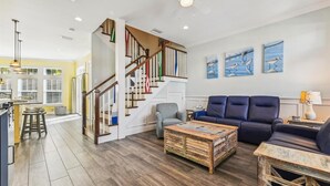 A spacious living room with a wooden coffee table, a blue sofa, and a staircase with colorful railings. - Beautiful Home Two Houses from the Beach!  Pool, Private Patio, 3 Bedrooms (Holmes Beach)