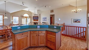 A spacious kitchen with a large island, wooden cabinets, and a dining area with chairs. - Paws and Reflect - Corolla, Ocean Sands, 200 Yds to Beach, Pool, Hot Tub, Pool Table, Pets OK (Corolla)