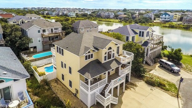 A multi-story house with a large deck, a swimming pool, and a view of a lake. - Paws and Reflect - Corolla, Ocean Sands, 200 Yds to Beach, Pool, Hot Tub, Pool Table, Pets OK (Corolla)