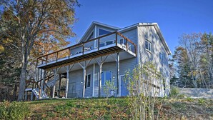 Uma casa de dois andares com varanda, rodeada por árvores e um gramado.