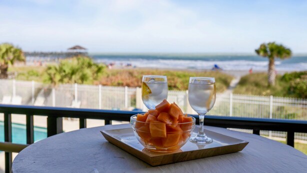 Une table avec un saladier de fruits et deux verres sur un plateau, donnant sur une plage.