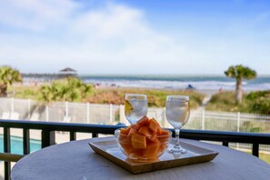 A table with a bowl of fruit and two glasses on a tray, overlooking a beach. - Oceanfront Condo Near Pier with Views & Heated Pool (Cocoa Beach)