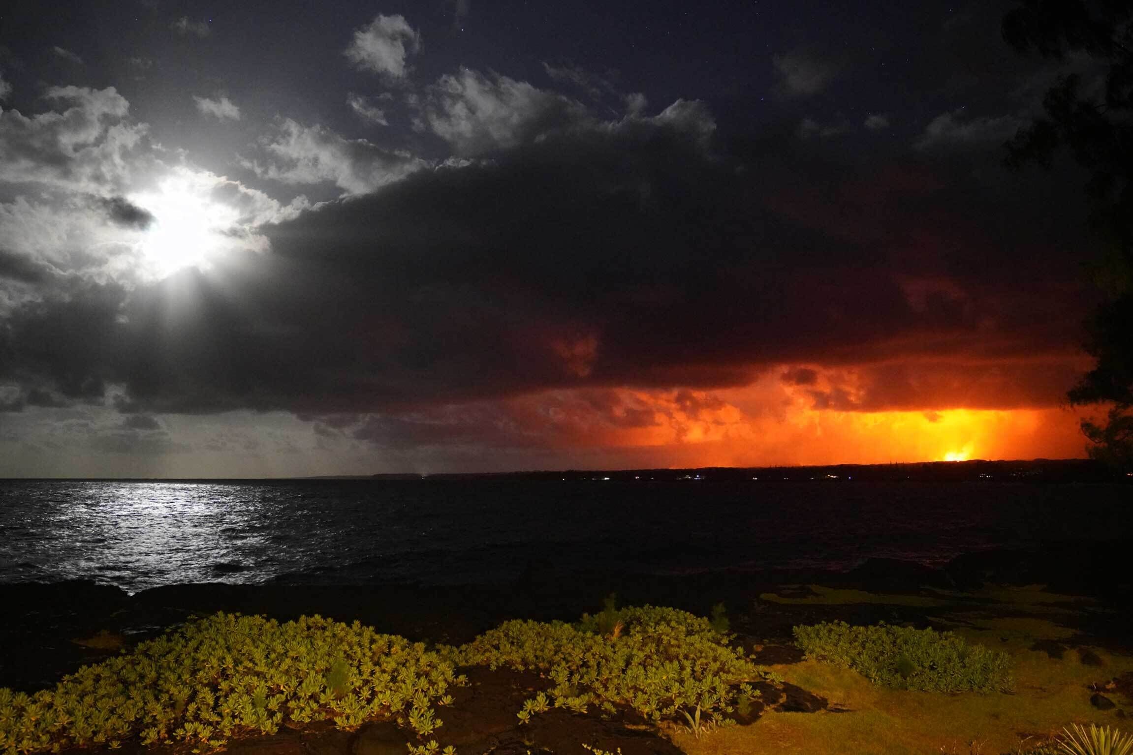 Een nachtelijke scène met een heldere maan en een zonsondergang boven de oceaan, met beplanting op de voorgrond.