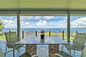 Un espacio de estar techado al aire libre con una mesa y sillas, con vista a una playa y el océano.