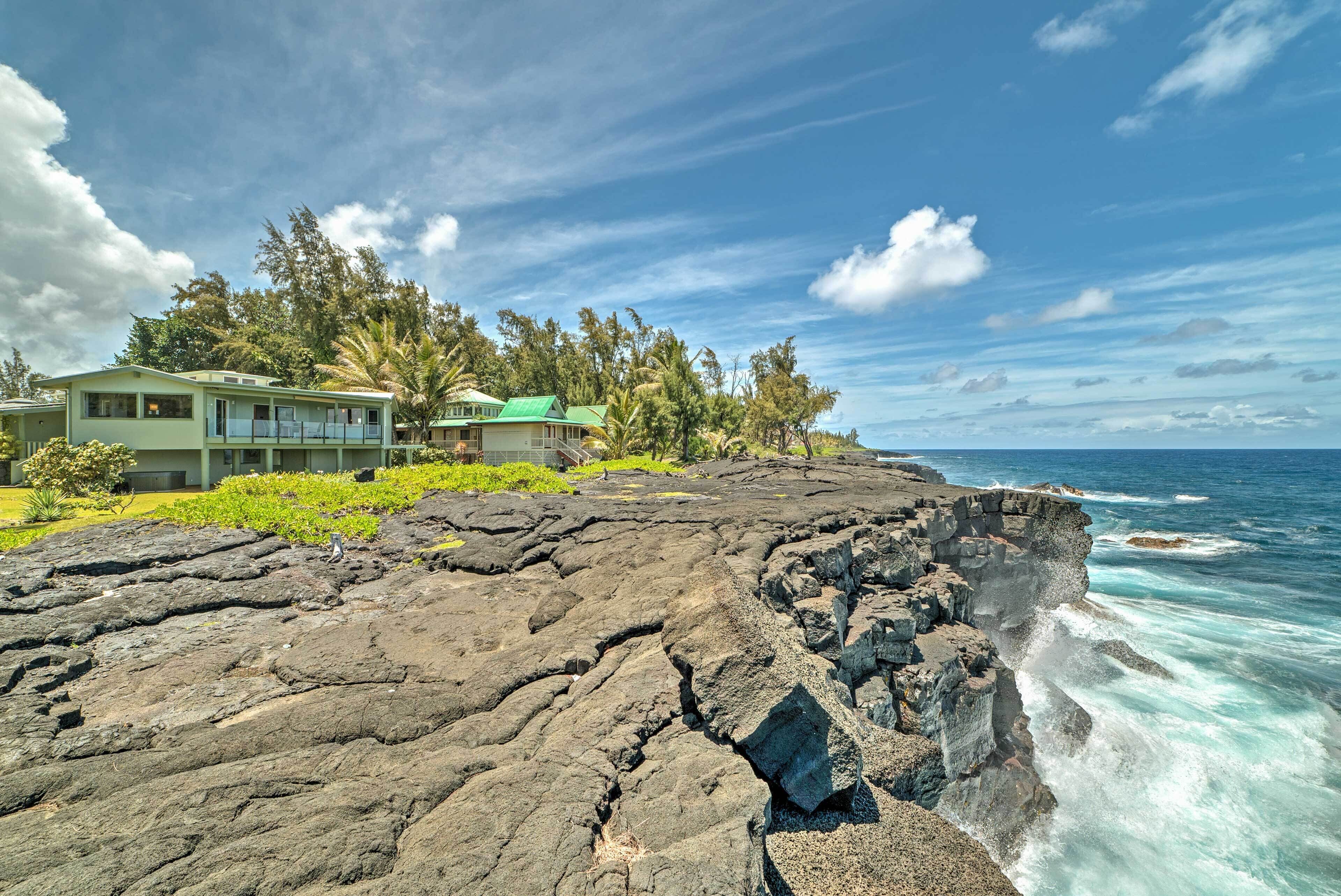 A coastal property with a house overlooking the ocean, featuring a rocky shoreline and lush greenery.