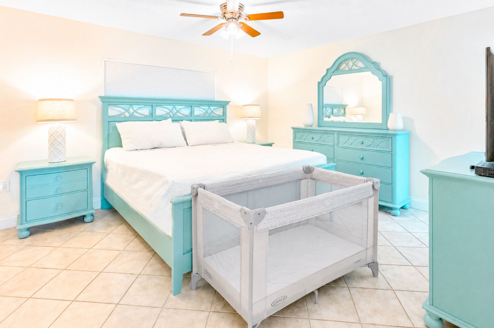 A bedroom with a bed, nightstands, a dresser, a crib, and a ceiling fan.
