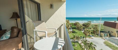 A balcony with a white table and two chairs, overlooking a beach and a golf course.