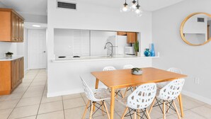 Una cocina moderna con armarios blancos, una mesa de comedor de madera con cuatro sillas y una isla integrada con fregadero.