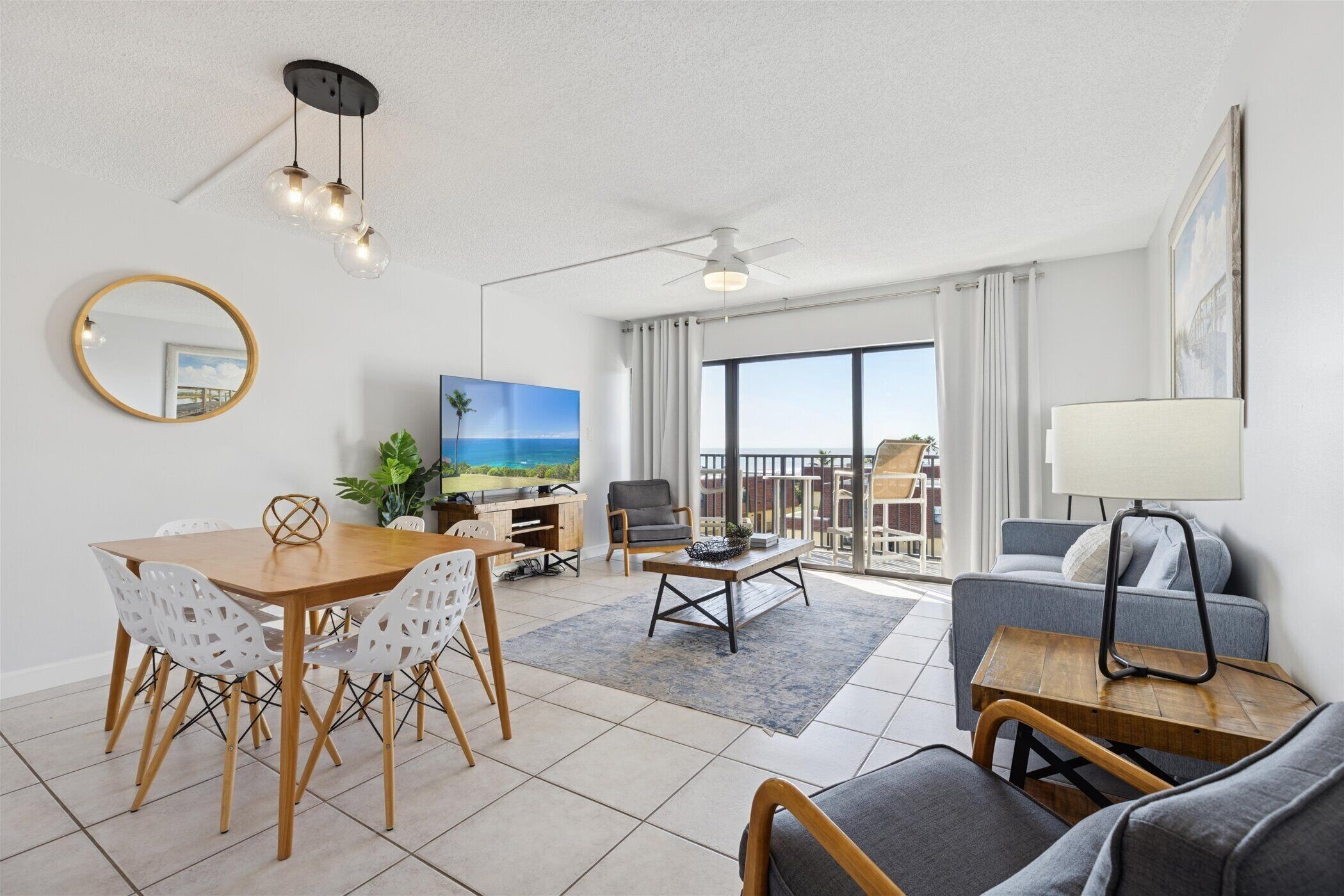 A modern living room with a dining area, a ceiling fan, a large window with a view, and a balcony.