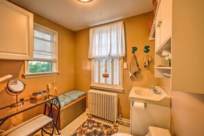 A compact bathroom with a radiator, a sink, a toilet, a bench, and a window with blinds. - Whimsical Lancaster Home - 4 Mi to Sight & Sound (Lancaster)